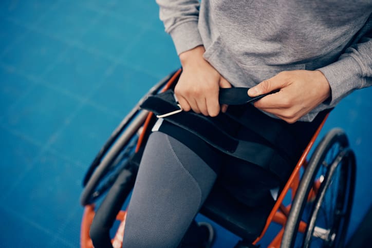 Unrecognizable athlete fastening belt on wheelchair while preparing to exercise on an outdoor court.